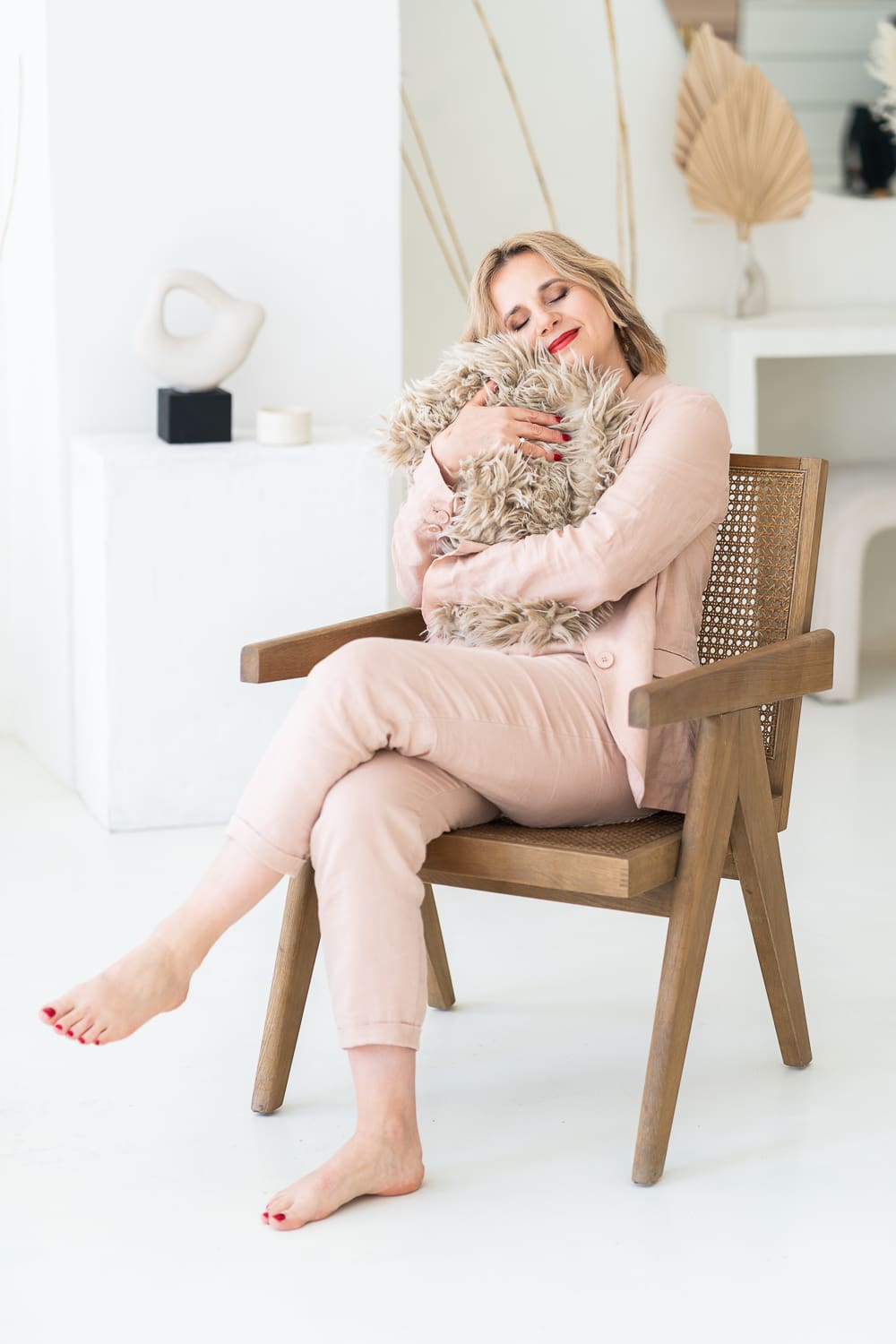 žena sedící na hnědém dřevěném křesle, v náručí drží stočenou kožešinu a vyzařuje laskavost