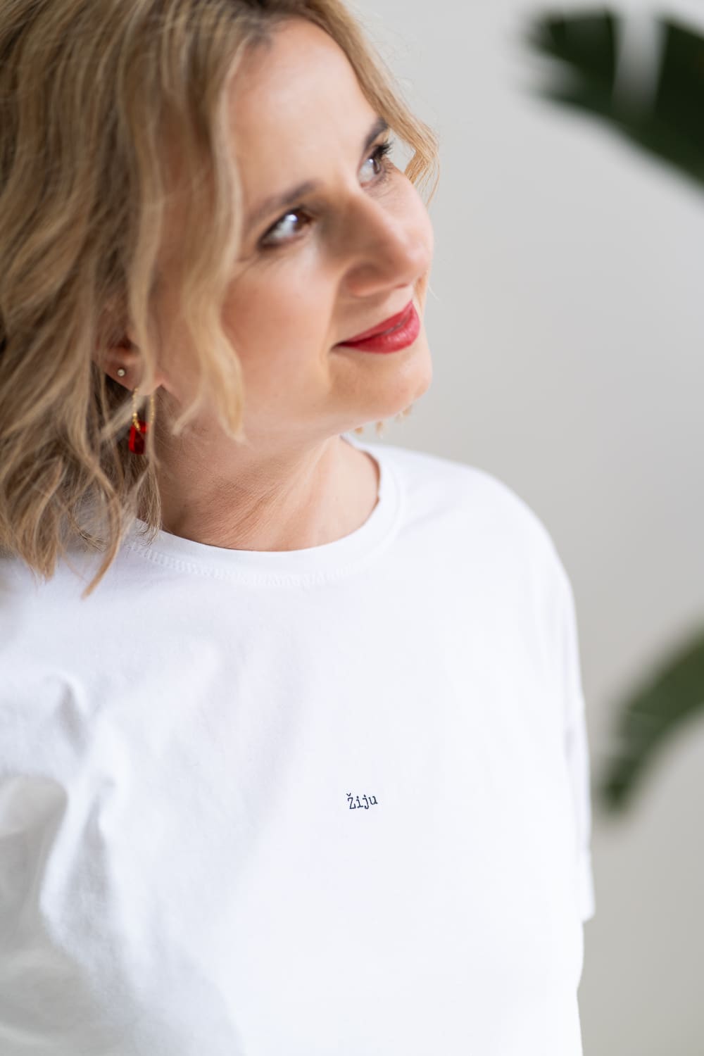 žena v bílém tričku s malým nápisem "žiju" se usmívá a dívá se směrem ven z fotky